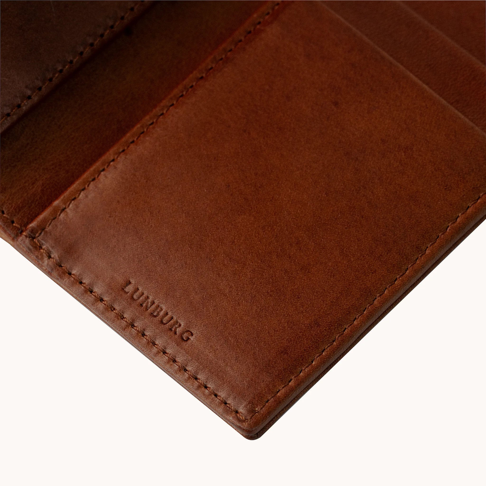 Lunburg Signet Vertical Bifold in Deep Mahogany, detail view of the interior lower panel showing the heat-embossed Lunburg mark beneath card slots, in vegetable-tanned Perpetual Leather (from Tempesti) with folded edge construction throughout.