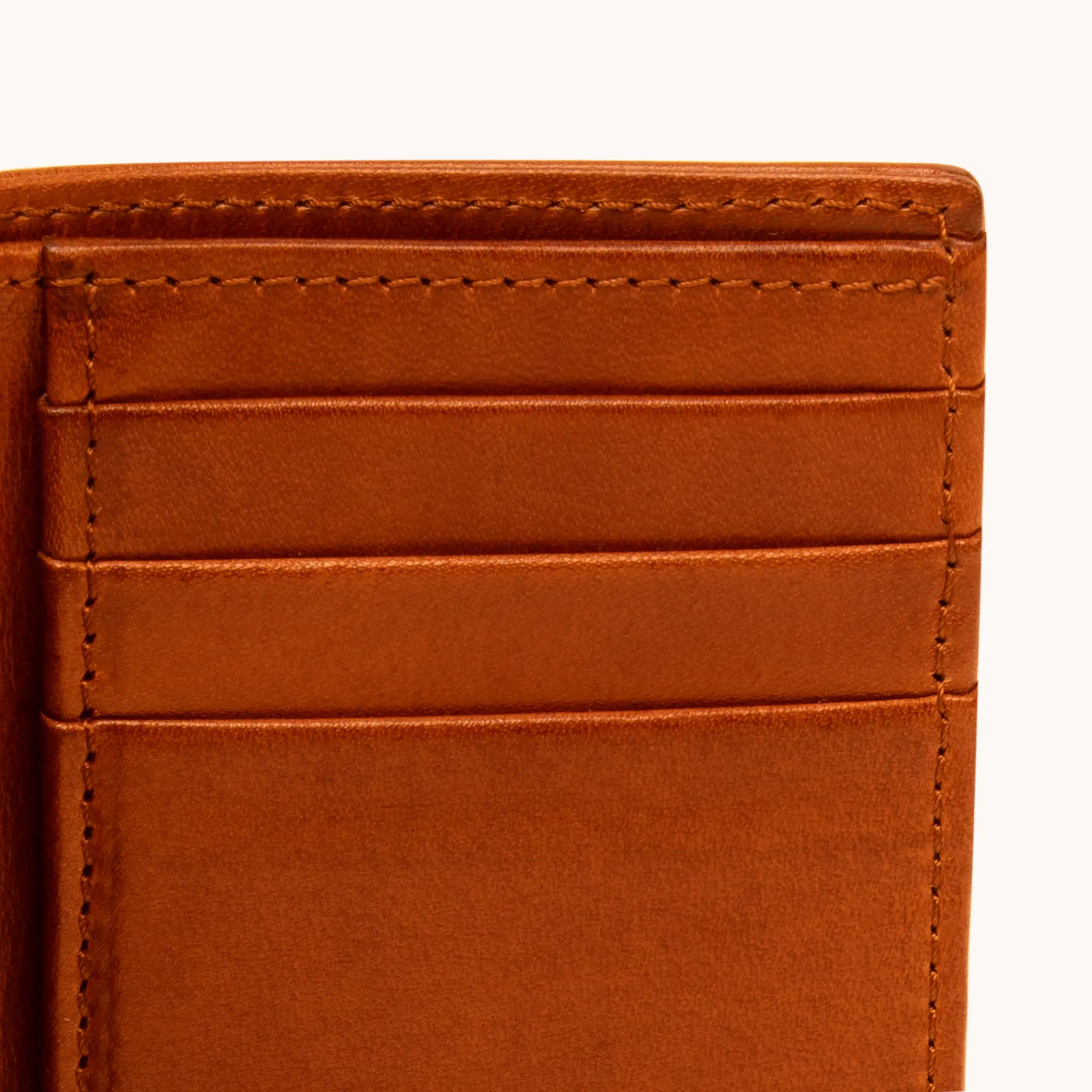 Close-up of card slot stitching on the Lunburg Vertical Bifold Wallet in Heritage Amber, showing precise stitch lines, folded edge construction, and leather grain in vegetable-tanned Perpetual Leather.
