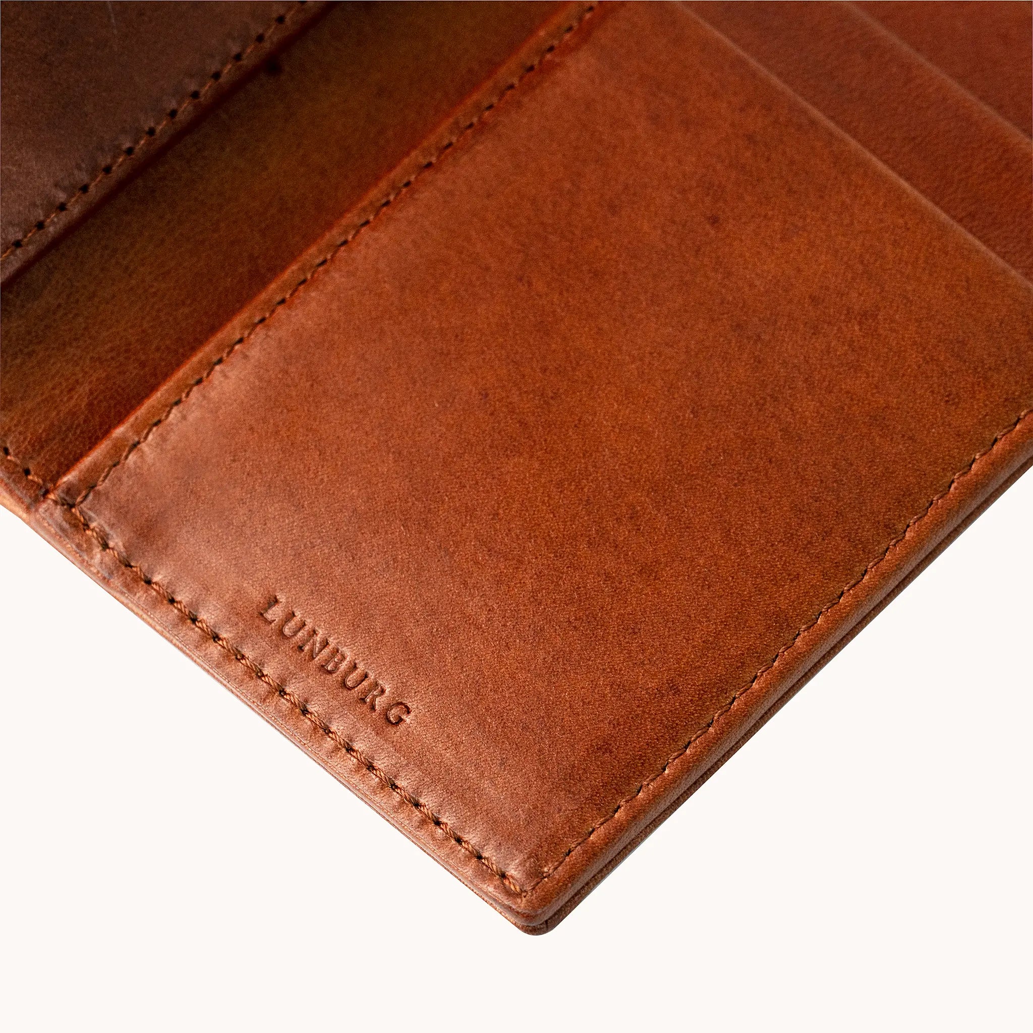 Close-up of the heat-embossed Lunburg mark on the interior of the Vertical Bifold Wallet in Heritage Amber, with folded edge construction, card slot edges, and saddle stitching visible above, in vegetable-tanned Perpetual Leather.