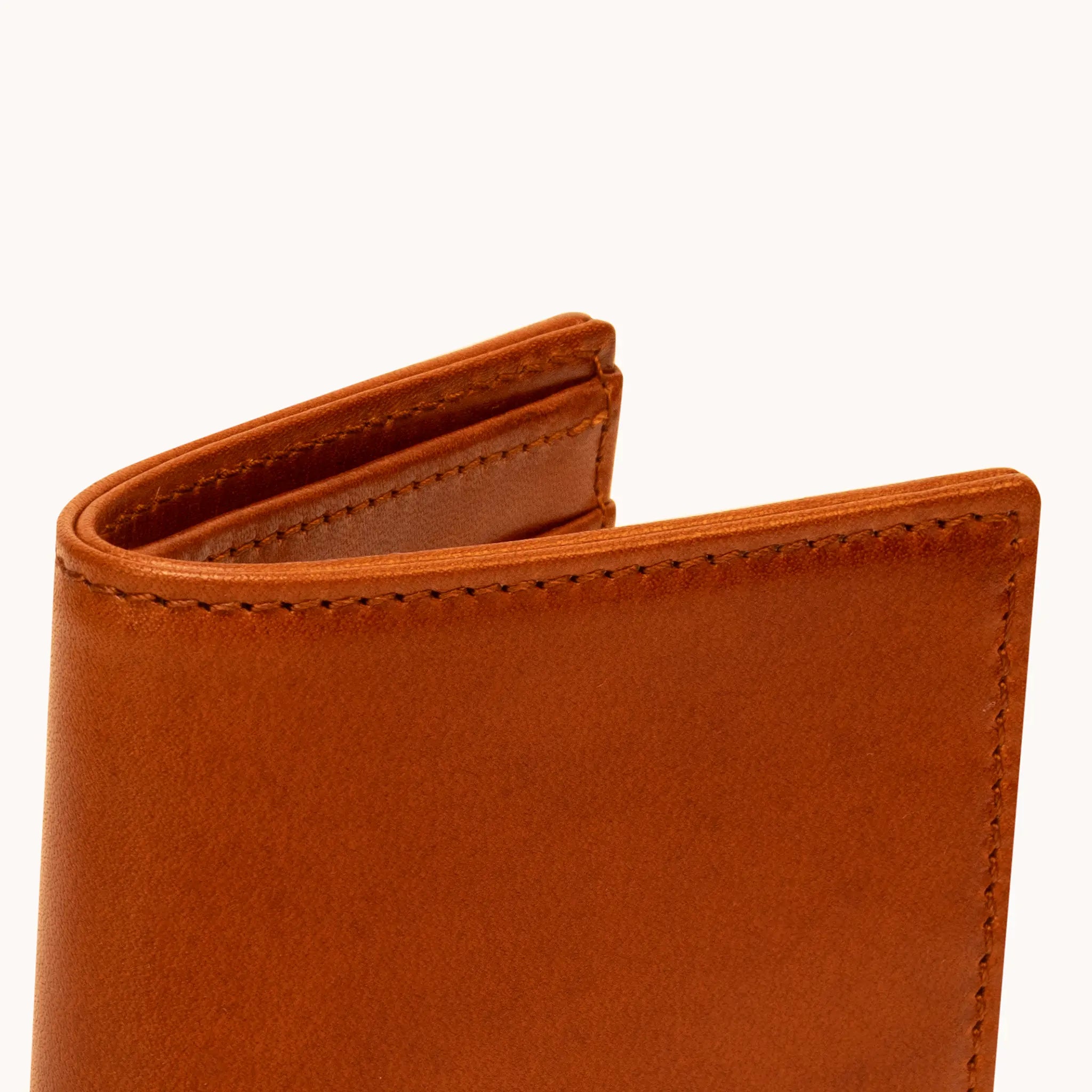 Close-up of the upper spine and fold of the Lunburg Vertical Bifold Wallet in Heritage Amber, showing folded edge construction, edge stitching, and interior glimpse in vegetable-tanned Perpetual Leather.