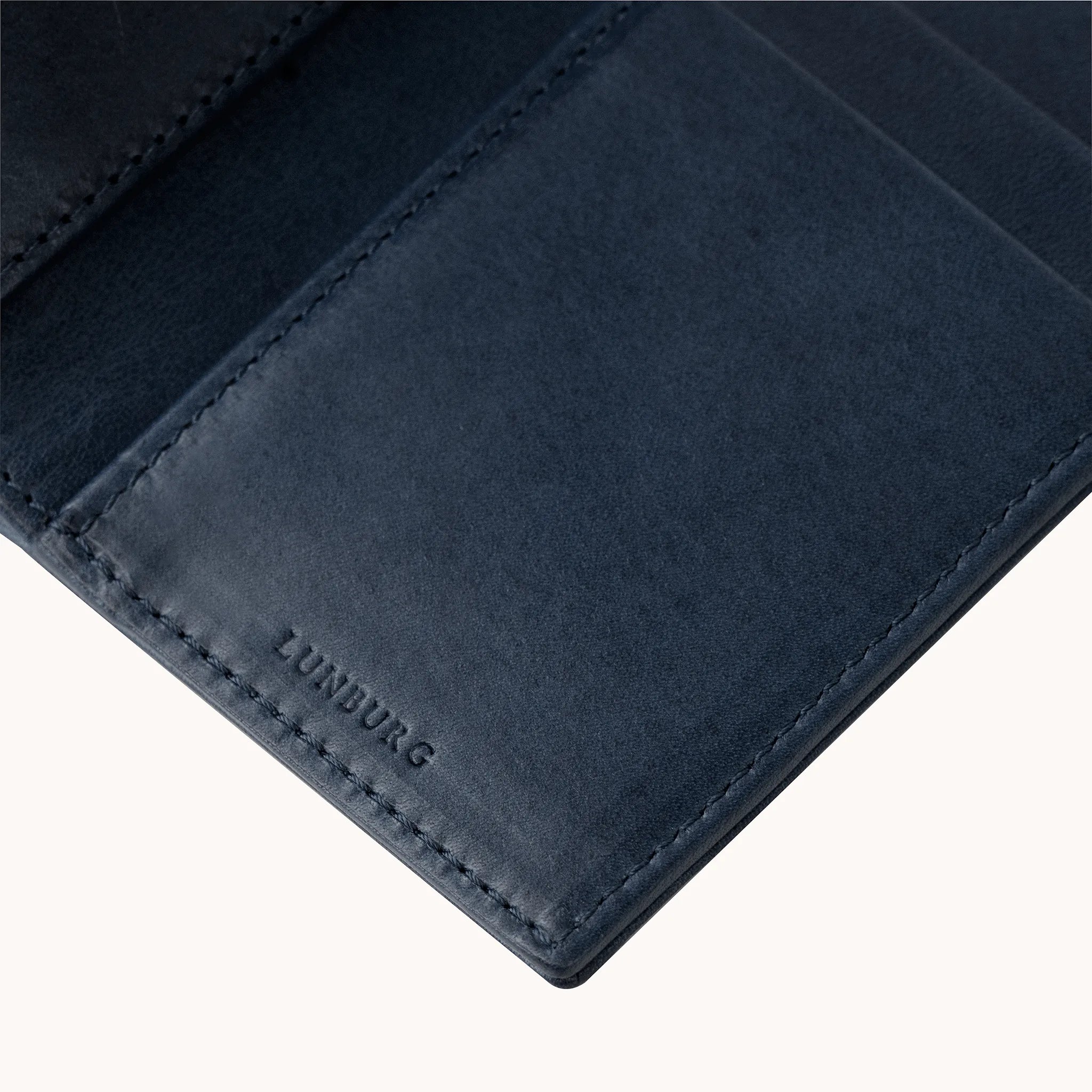 Lunburg Signet Vertical Bifold in Nocturnal Sapphire, detail view of the interior lower panel showing the heat-embossed Lunburg mark beneath card slots, in vegetable-tanned Perpetual Leather (from Tempesti) with folded edge construction throughout.